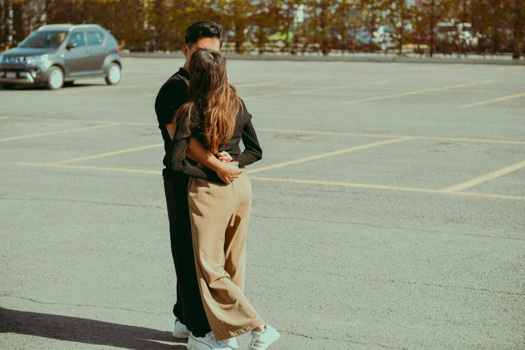 A couple warmly embrace in a sunlit empty parking lot, expressing love.